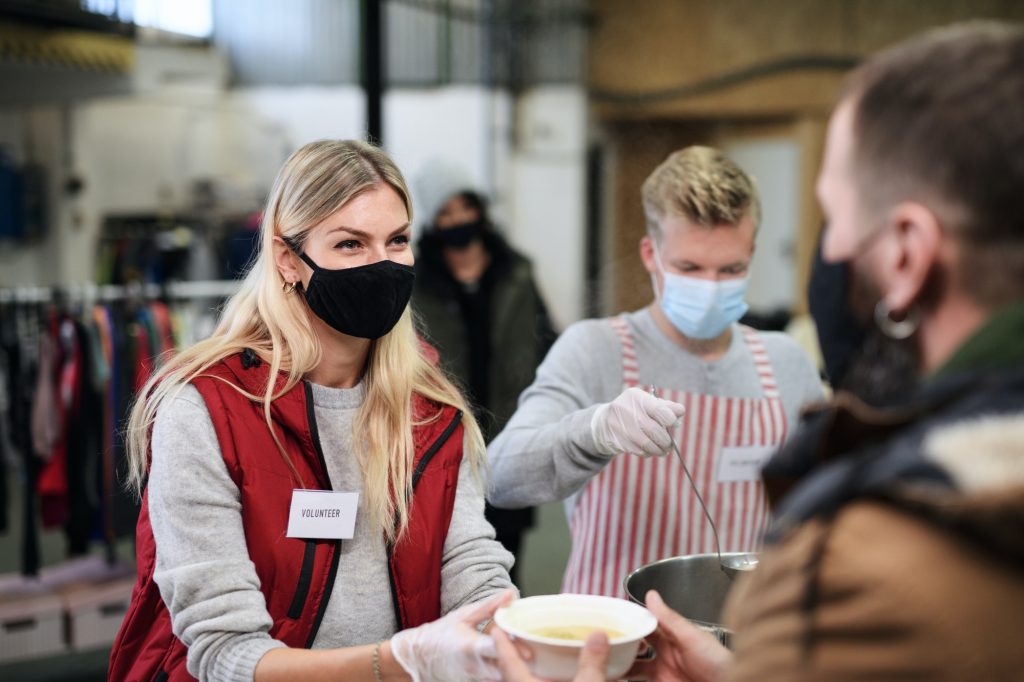 Volunteers serving hot soup for homeless in community charity donation center, coronavirus concept.